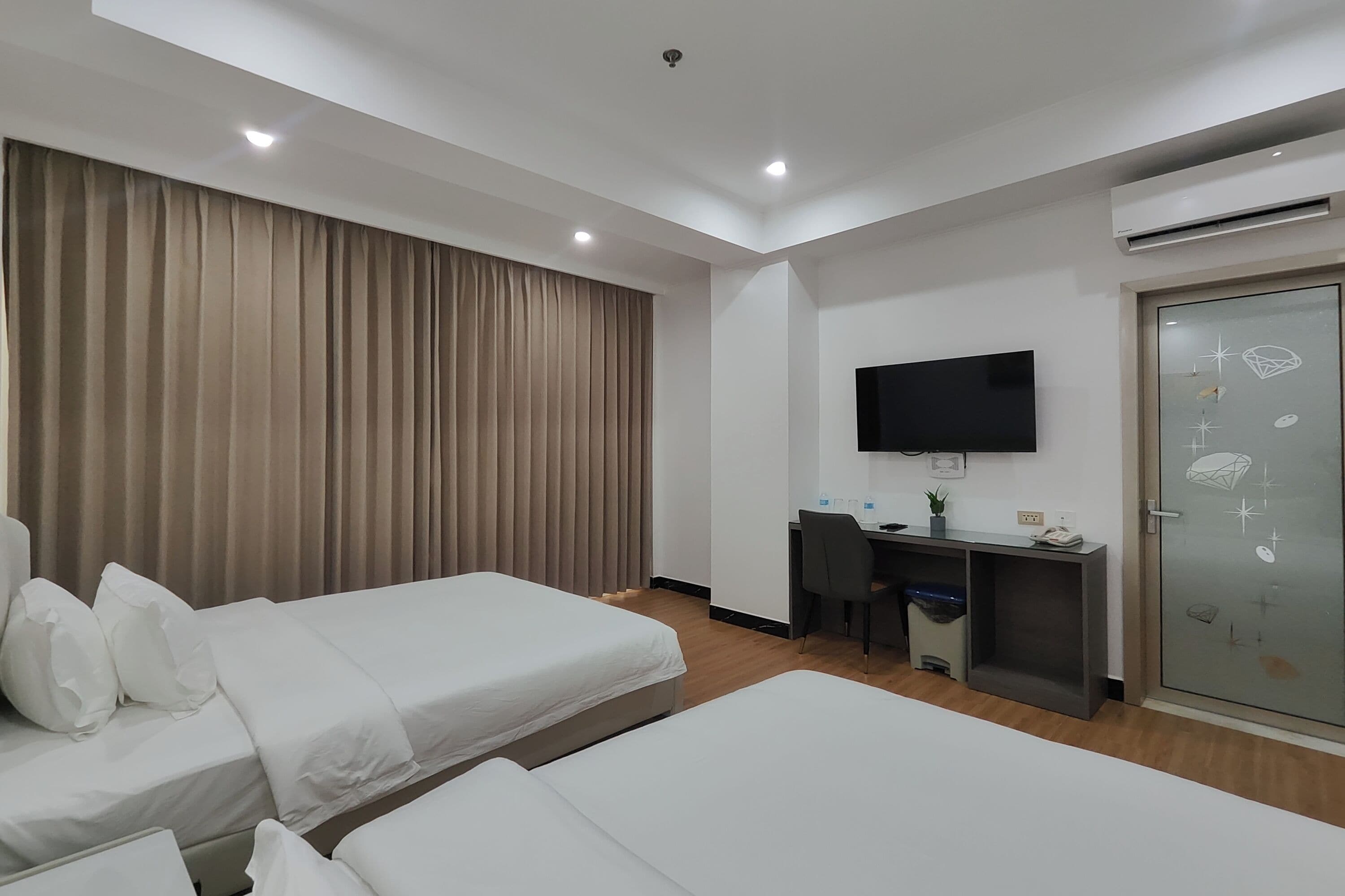 A hotel room with two beds, a desk, a television, and an air conditioning unit.