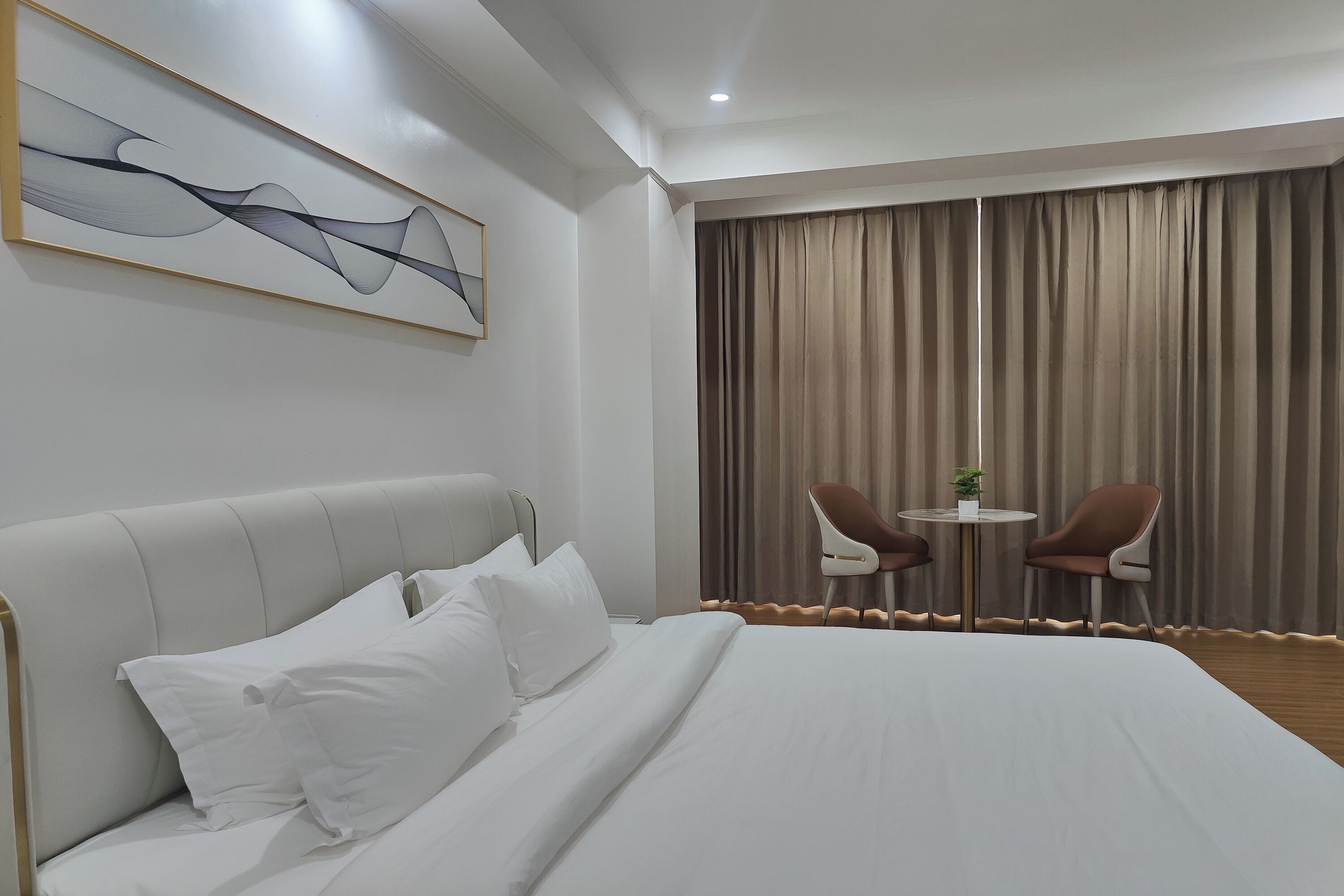 Camera d'albergo con un letto grande, una testiera, due poltrone, un tavolino, un quadro appeso al muro e una finestra con tende.