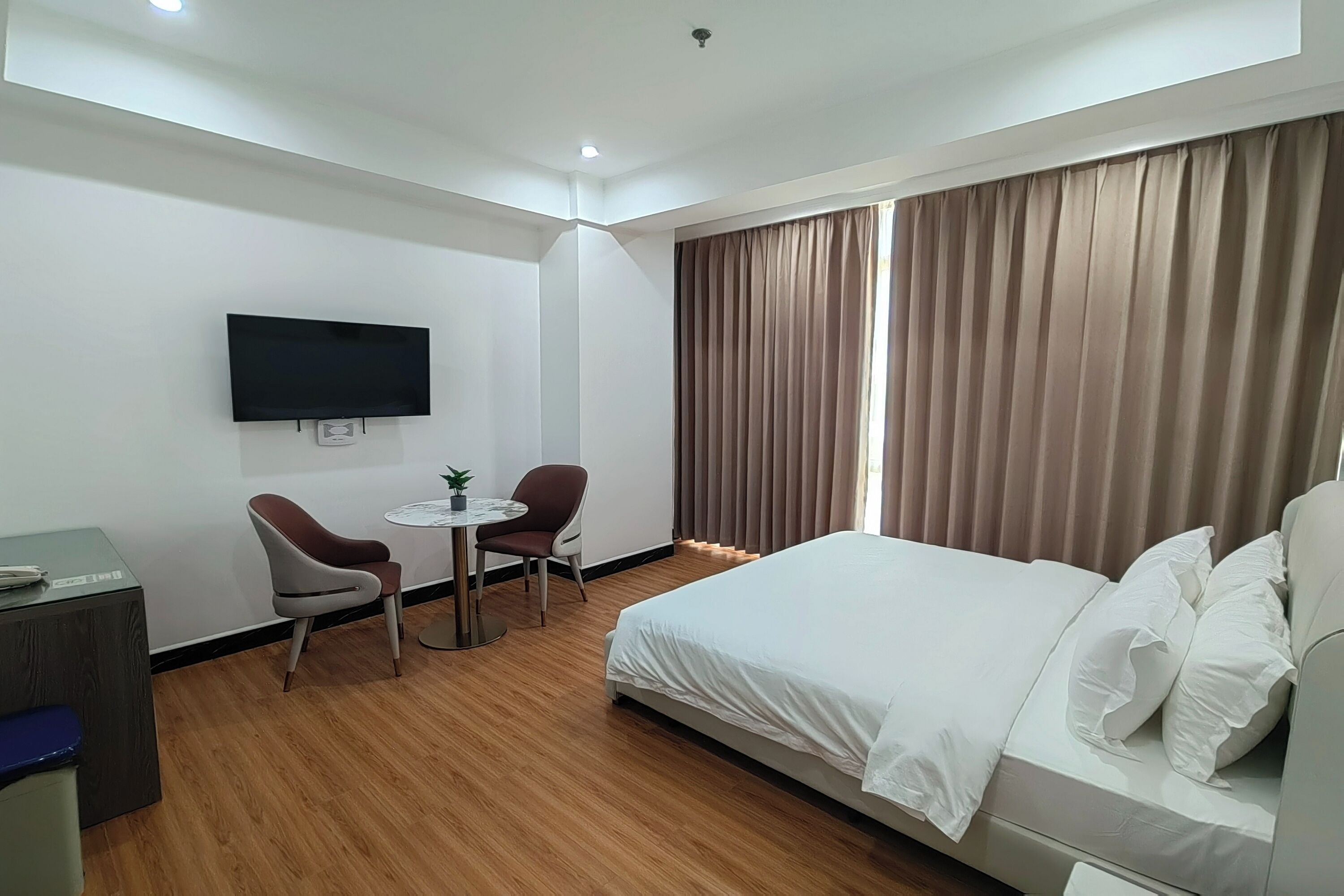 Habitación de hotel con cama, escritorio, dos sillas, televisor y ventana con cortinas.