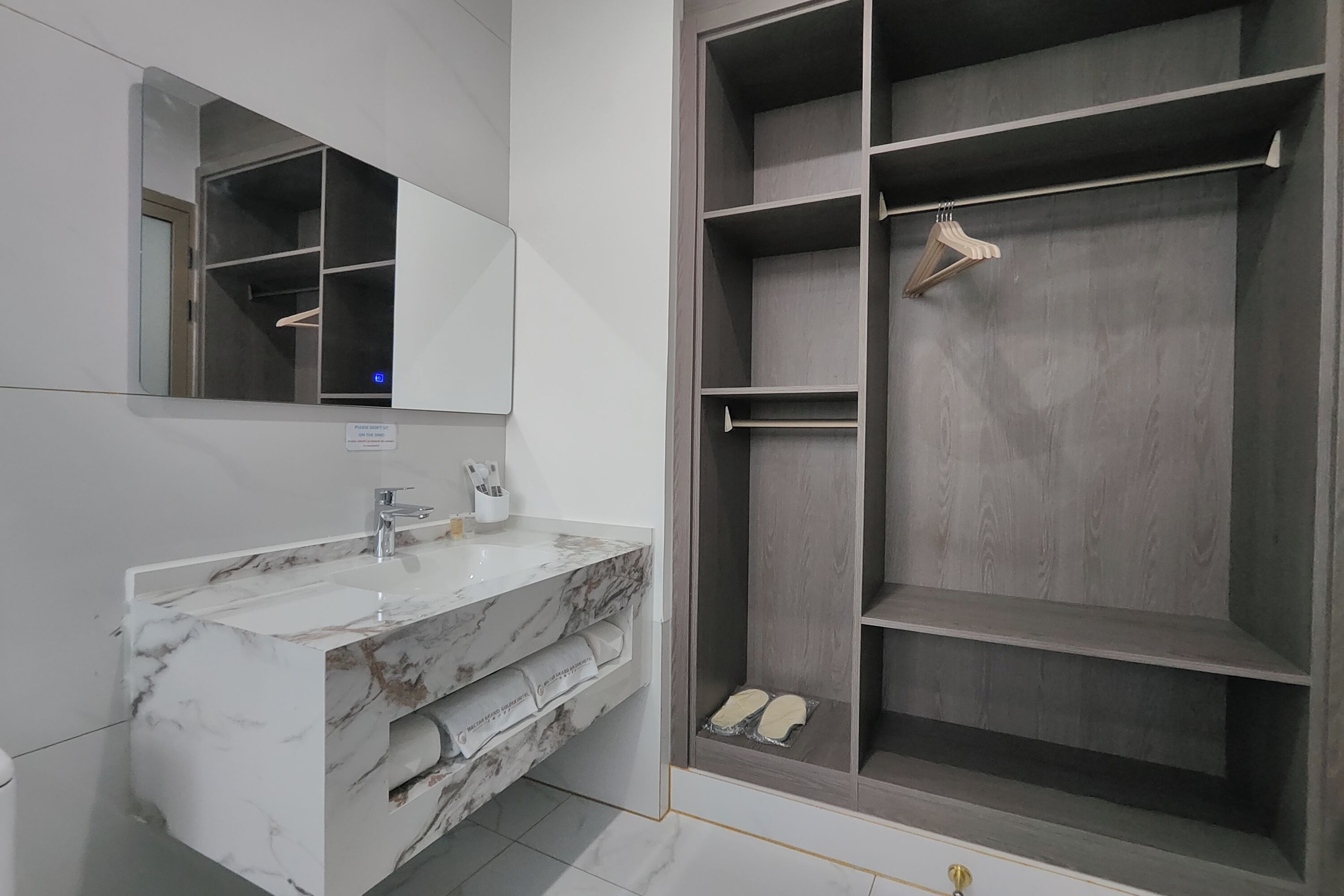 A modern bathroom with a marble sink, a large mirror, and a walk-in closet with shelves and a hanging rack.