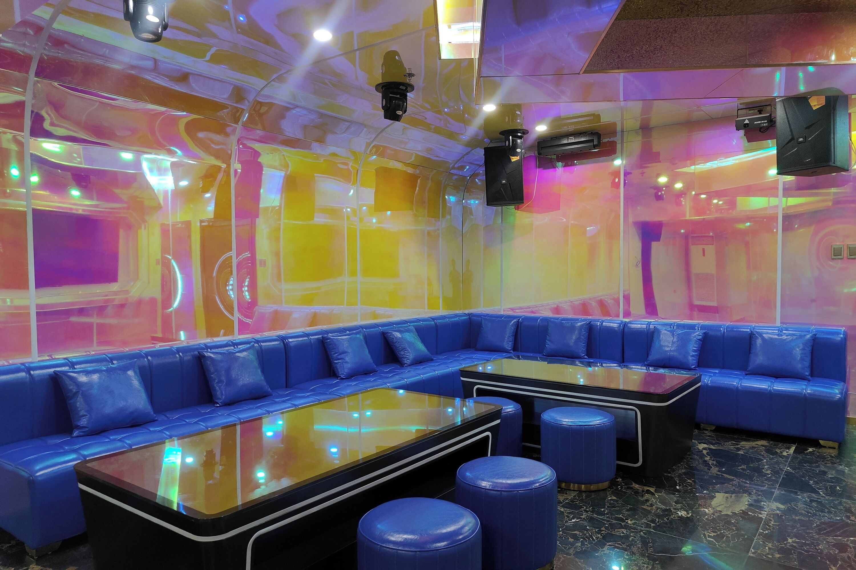 A modern lounge area with a blue leather sofa, a glass-top table, and blue stools.