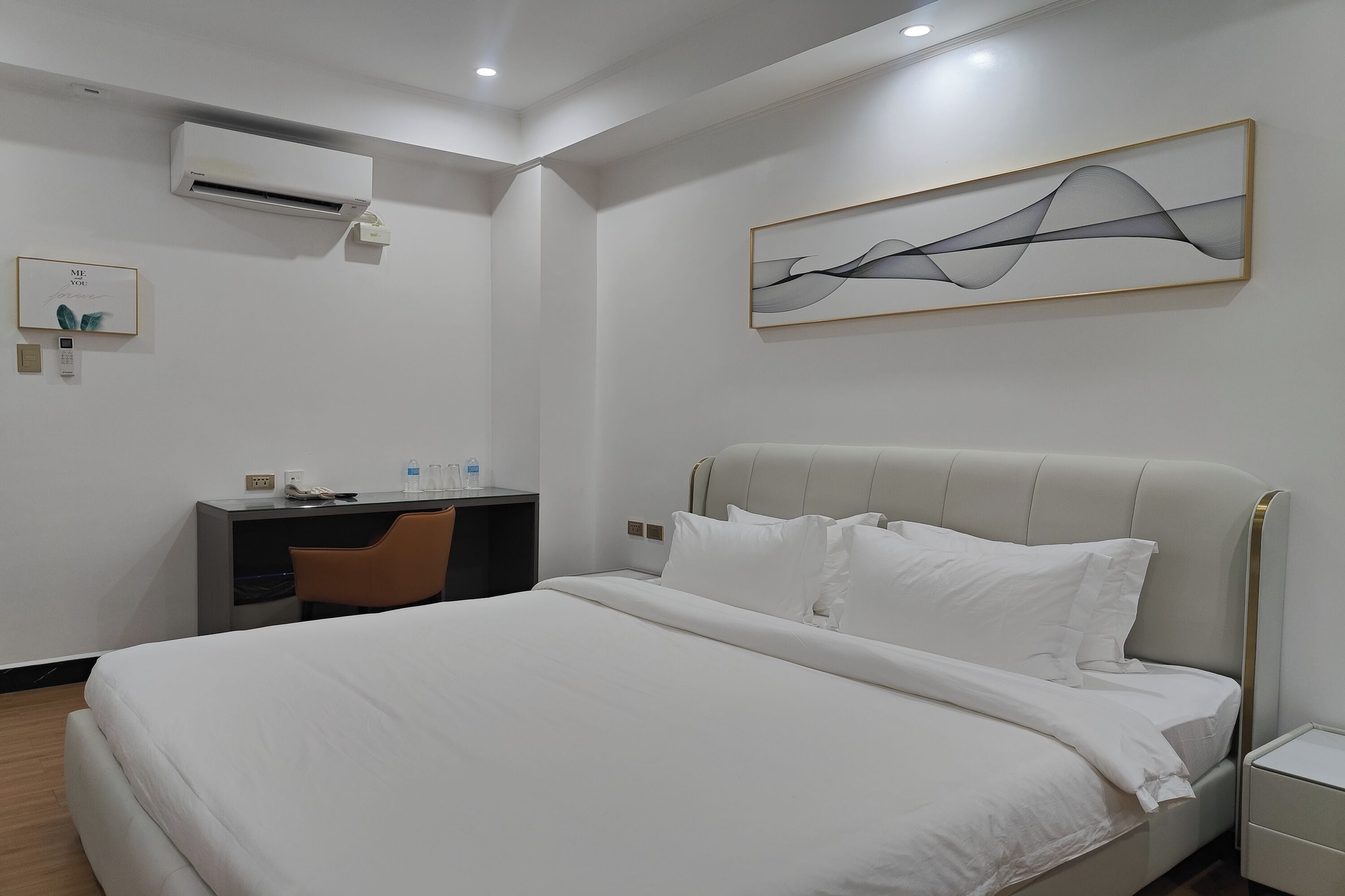 A hotel room with a bed, a desk, and an air conditioning unit.