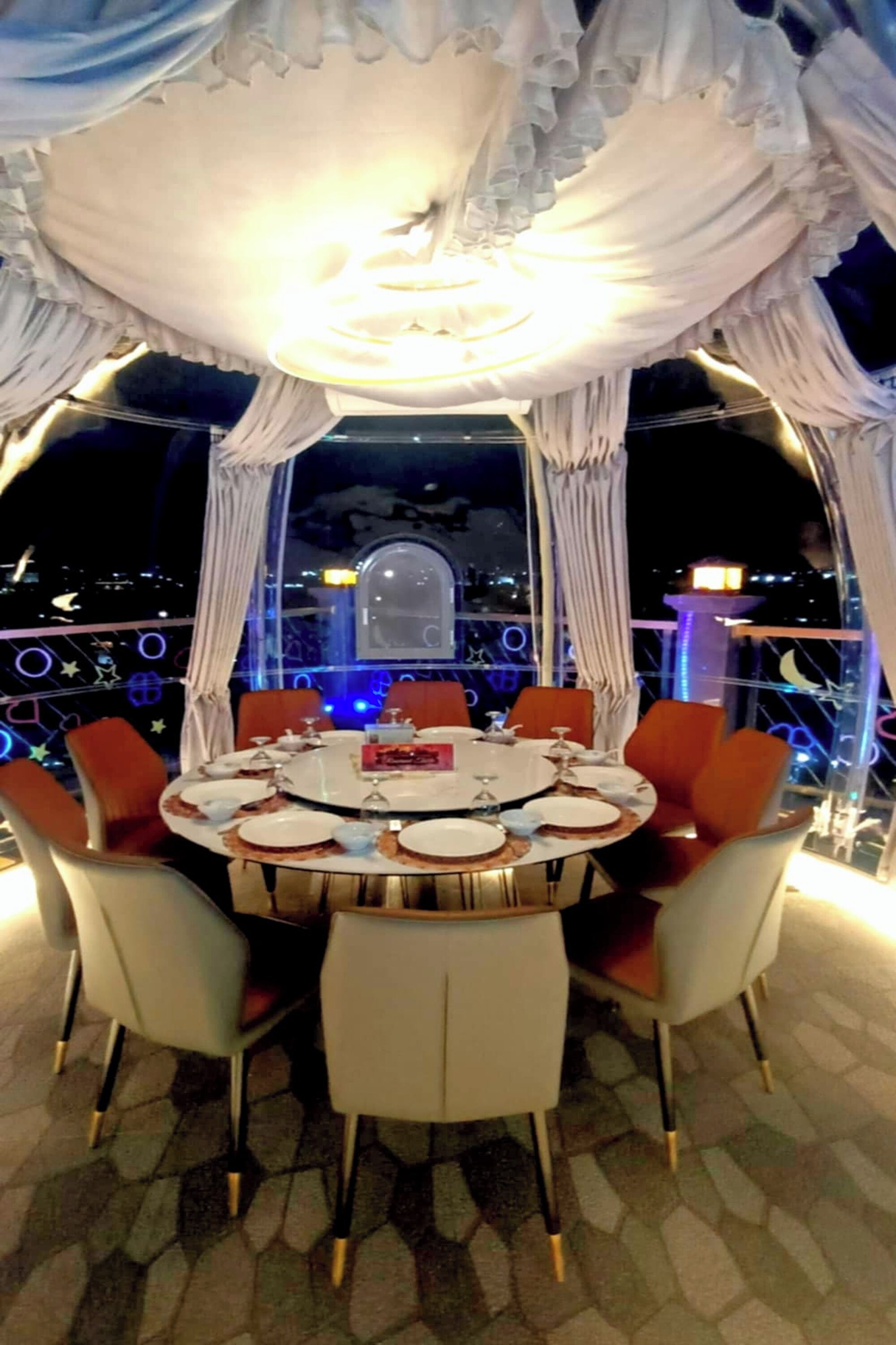 A dining area with a round table set for six, surrounded by chairs with a mix of white and orange upholstery.