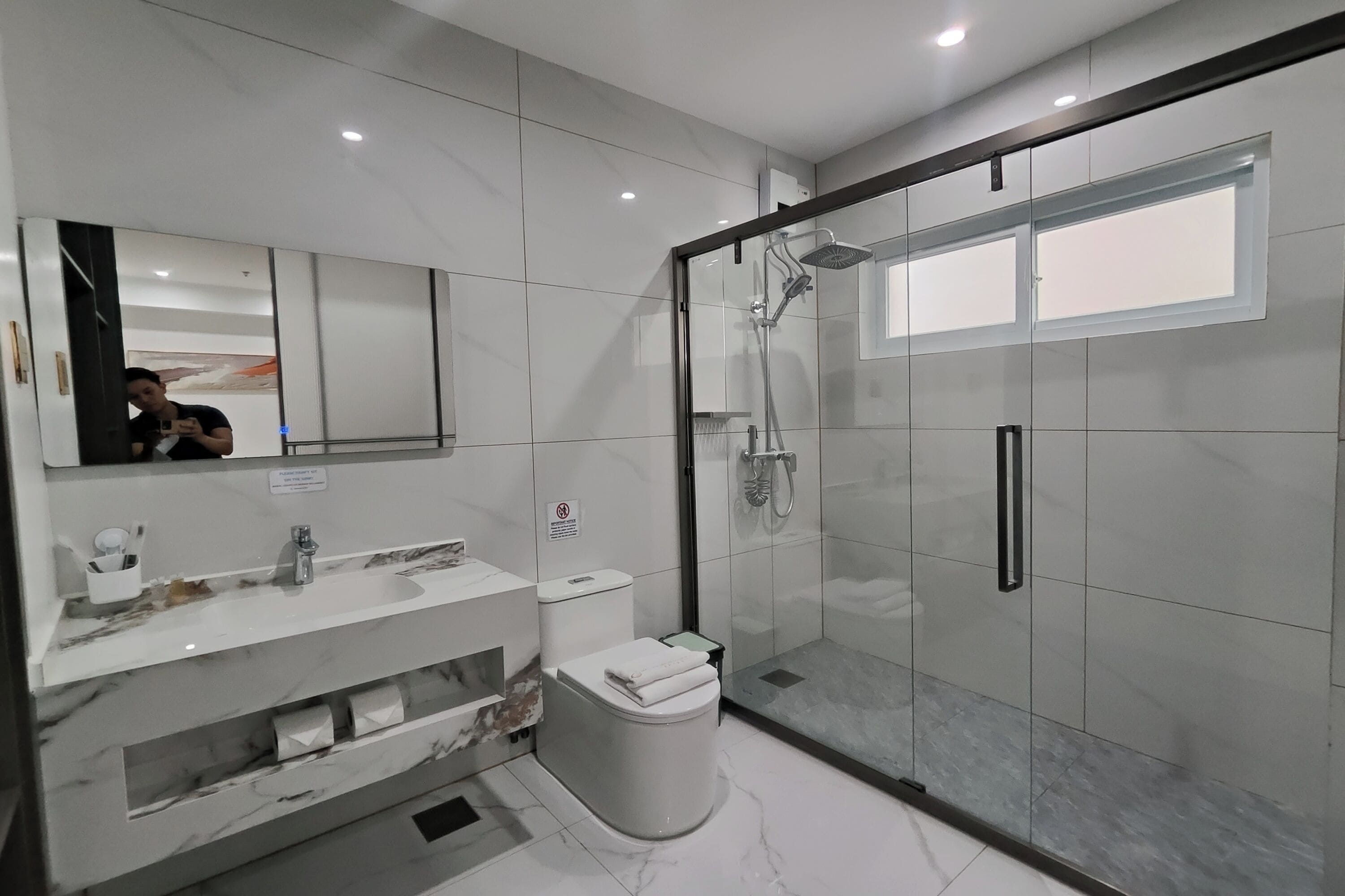 A modern bathroom with a glass-enclosed shower, a marble vanity, and a toilet.