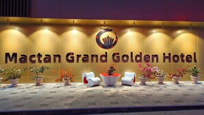 Fachada del Mactan Grand Golden Hotel con un letrero llamativo, plantas en macetas y asientos modernos.