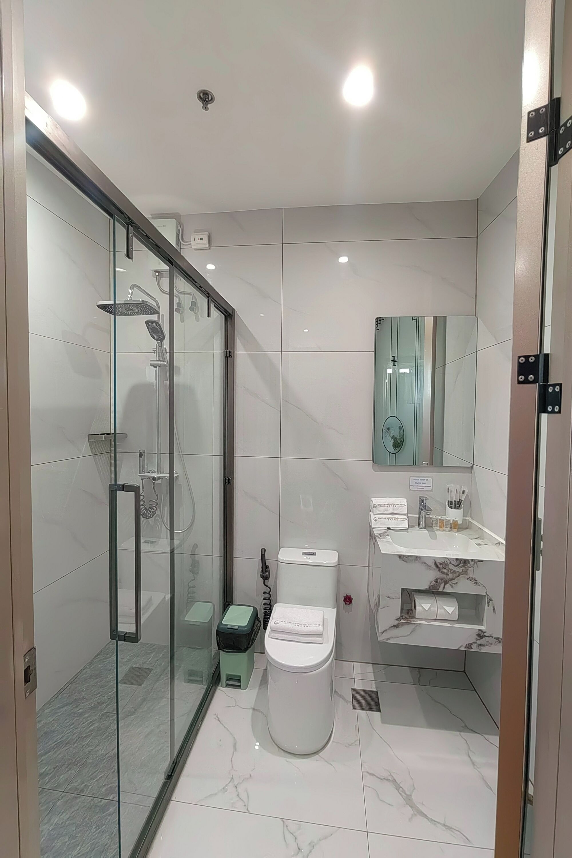 Een moderne badkamer met een douchecabine van glas, een wit toilet, een vloer van marmer en een wastafel met spiegel.