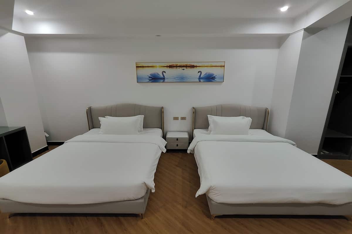 Una habitación de hotel con dos camas, una mesita de noche, un cuadro de cisnes en la pared y piso de madera.