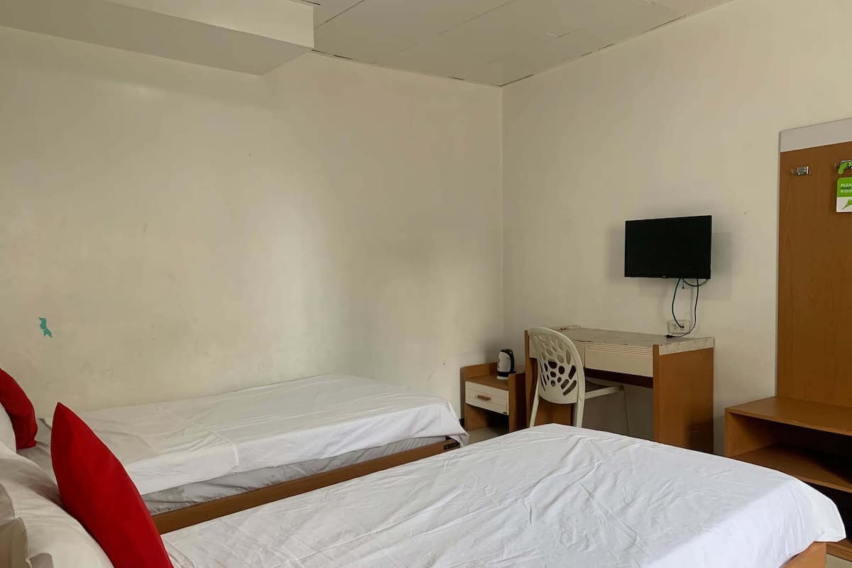 Ein Zimmer mit zwei Einzelbetten, einem Schreibtisch mit Stuhl, einem Fernseher und einem Holzschrank.