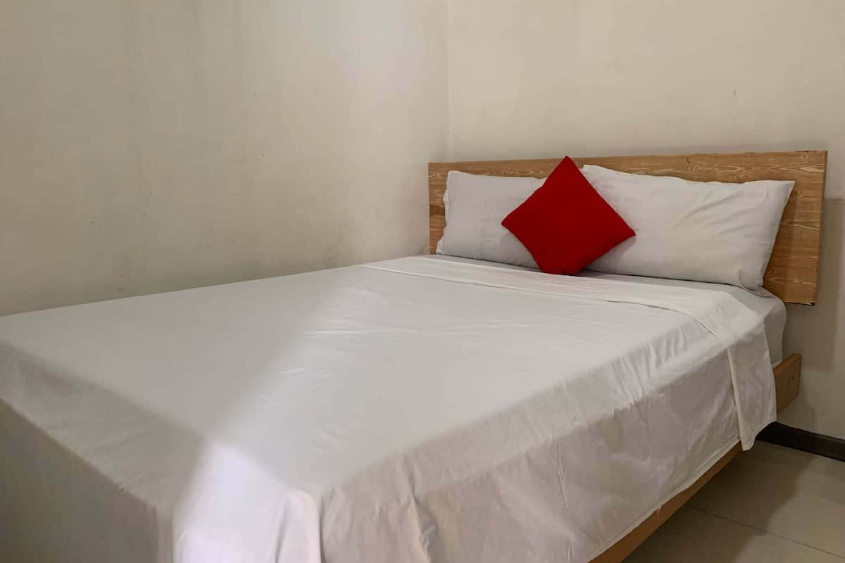 Ein Zimmer mit einem Einzelbett, einem hölzernen Kopfteil, weißer Bettwäsche und einem roten Kissen.