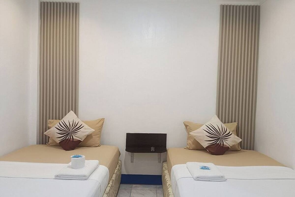A hotel room with two single beds, each with a pillow and a towel. There is a small table between the beds.