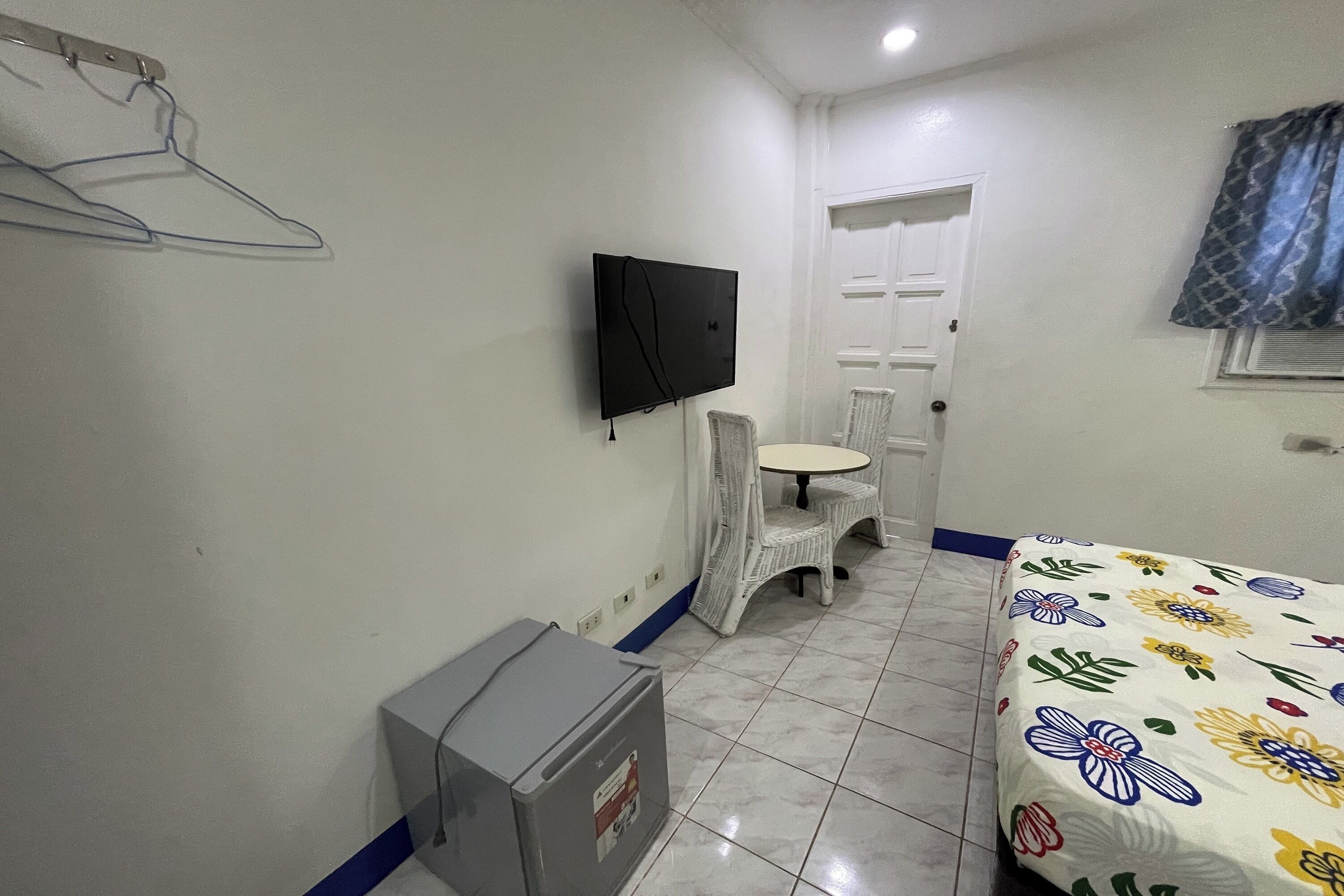 A small, clean room with a bed, a TV, a chair, and a small table.