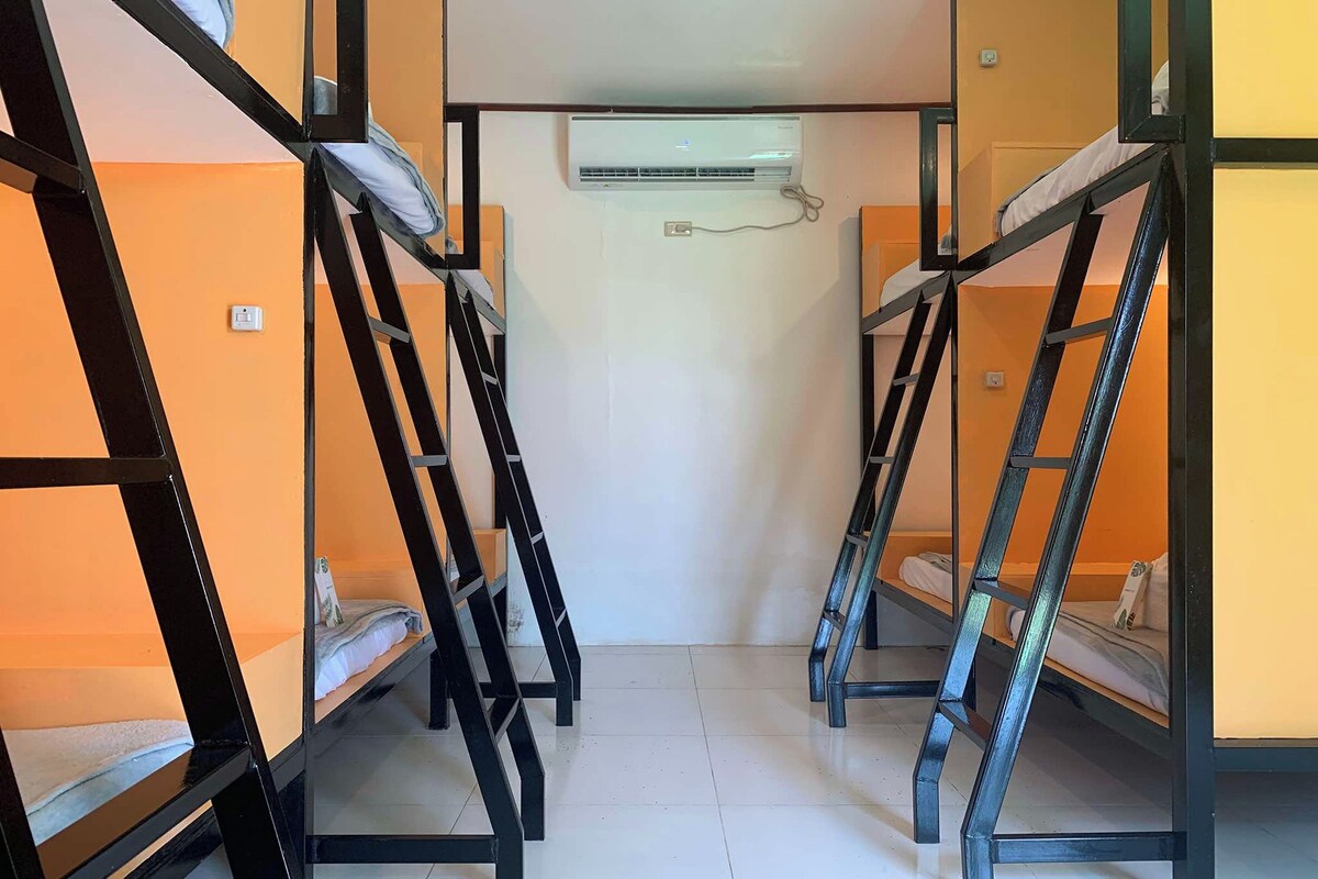 Une chambre de dortoir équipée de lits superposés, d’un appareil de climatisation et d’une prise électrique au mur.