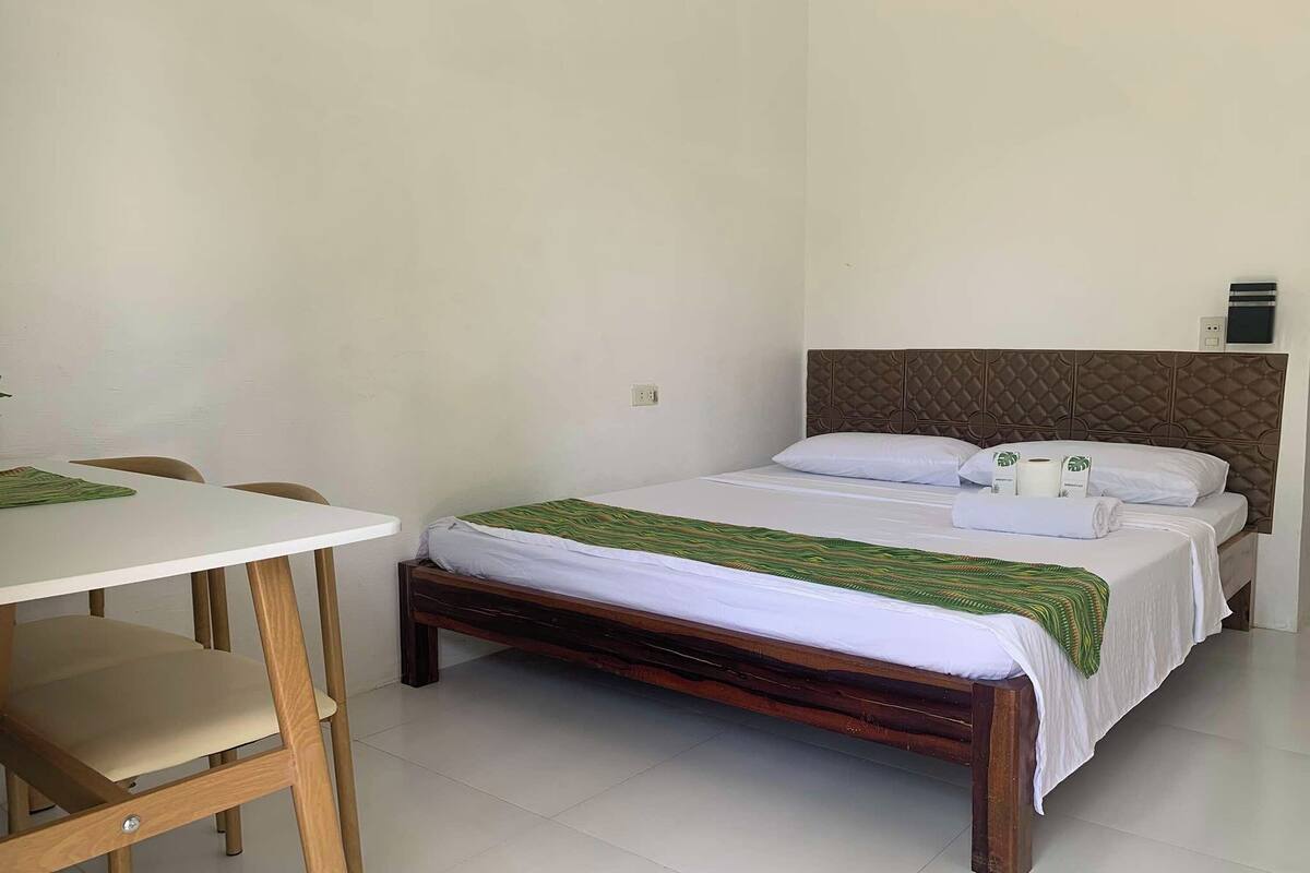 Een slaapkamer met een bed, een nachtkastje, een stoel en een klein tafeltje met een groene placemat.