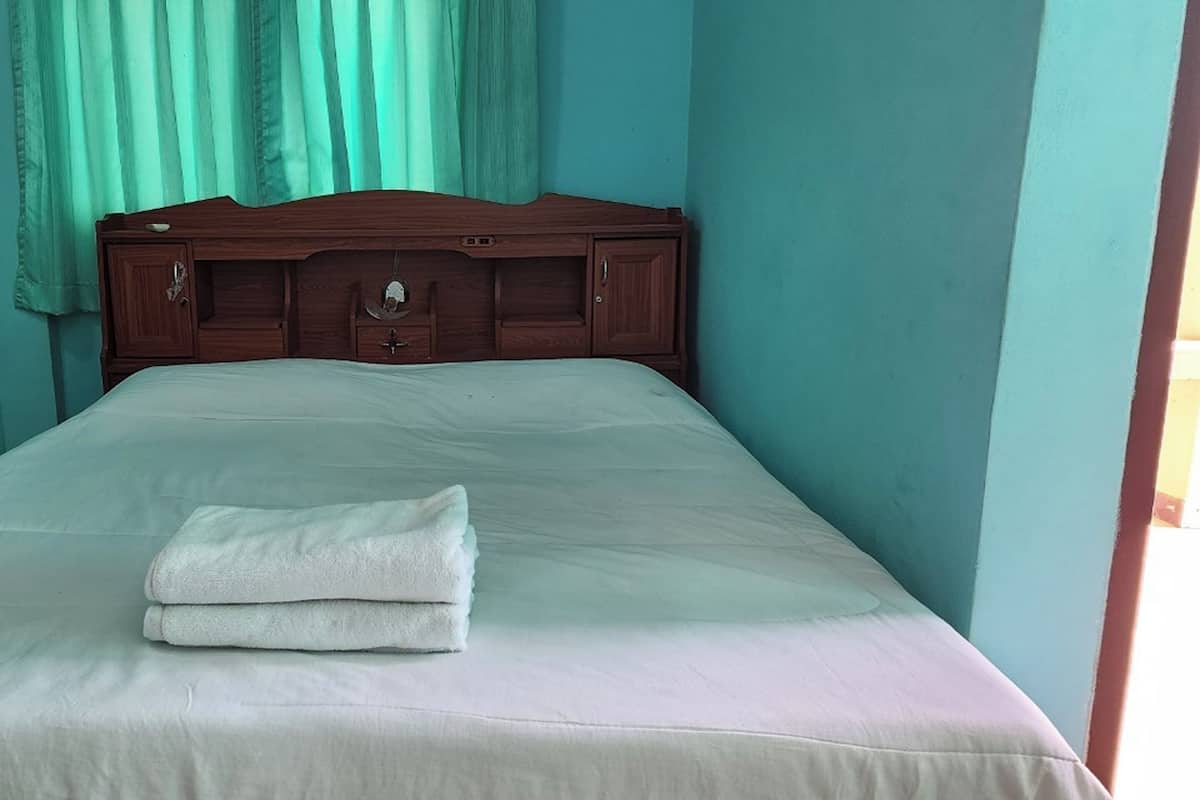 A single bed with a wooden headboard, a white bedspread, and a folded white towel on the bed.