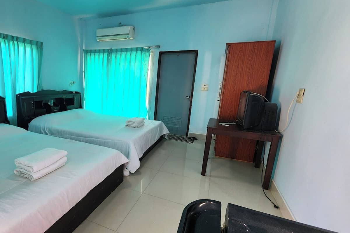 A hotel room with two beds, a desk with a television, and an air conditioning unit.