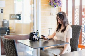 Une personne est assise à une table, avec un téléphone intelligent, un sac à main et un panneau affichant le menu en arrière-plan.