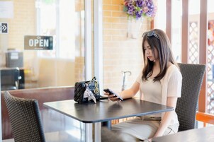 Una persona sentada a una mesa, con un teléfono inteligente, un bolso y un cartel de menú al fondo.