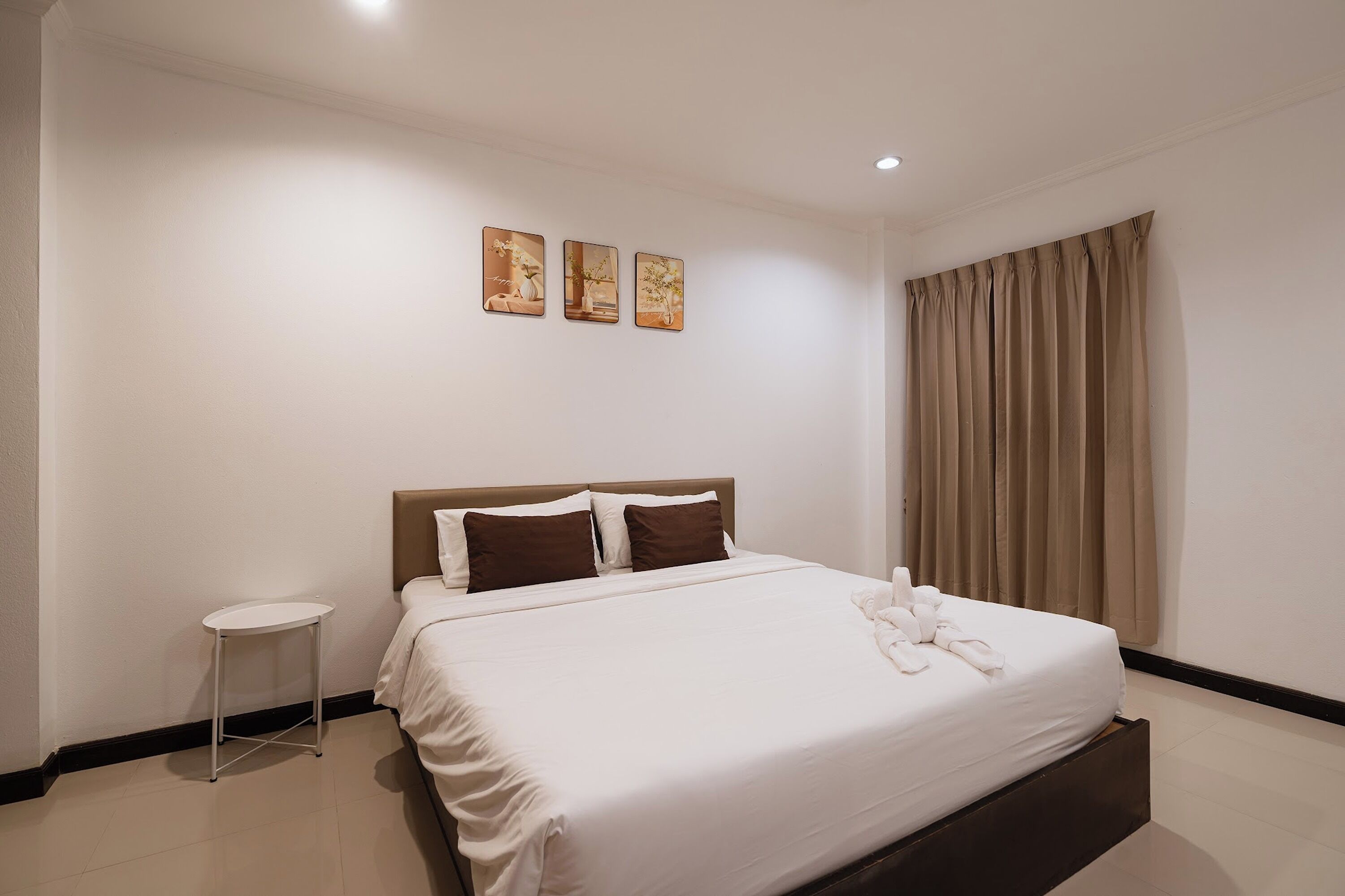 A hotel room with a bed, a bedside table, and a window with curtains.