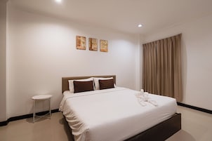 Una habitación de hotel con cama, mesita de noche y ventana con cortinas.