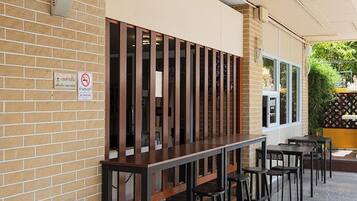An outdoor seating area with a brick wall, a no-smoking sign, and a covered section with tables and chairs.