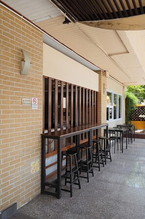 An outdoor seating area with a brick wall, a no-smoking sign, and a covered section with tables and chairs. - Jt Place Buriram (Buriram)