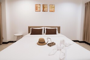 Une chambre d’hôtel avec un lit, des oreillers, un chapeau, un sac à main et une serviette.
