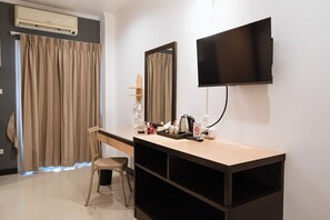 A hotel room with a flat-screen TV mounted on the wall, a desk with a chair, a vanity with a mirror, and a shower area with curtains. - Jt Place Buriram (Buriram)