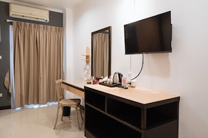 Habitación de hotel con televisor de pantalla plana montado en la pared, escritorio con silla, tocador con espejo y zona de ducha con cortinas.
