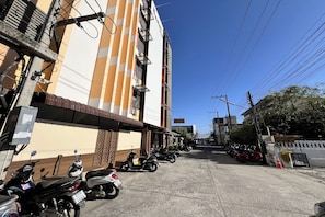 A street with parked motorcycles and a building with a striped facade. - Jt Place Buriram (Buriram)