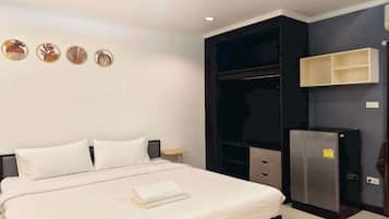 Habitación de hotel con cama, armario, mesita y refrigerador.