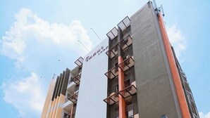 A multi-story building with a prominent sign, balconies, and a ground-level entrance with seating. - Jt Place Buriram (Buriram)
