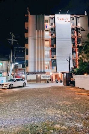 A multi-story building with a prominent sign, a gated entrance, and a white car parked in front. - Jt Place Buriram (Buriram)