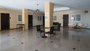 A spacious lobby with a polished floor, a central seating area with tables and chairs, and a clock on the wall. - Jt Place Buriram (Buriram)