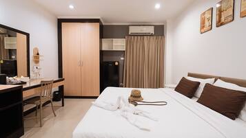 Habitación de hotel con cama, escritorio, silla, armario, unidad de aire acondicionado y cortina.