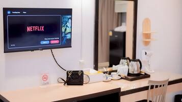 Habitación de hotel con una televisión mostrando la interfaz de Netflix, una cafetera, un hervidor de té, una mesita con un bolso y un cartel de 'NO FUMAR'.