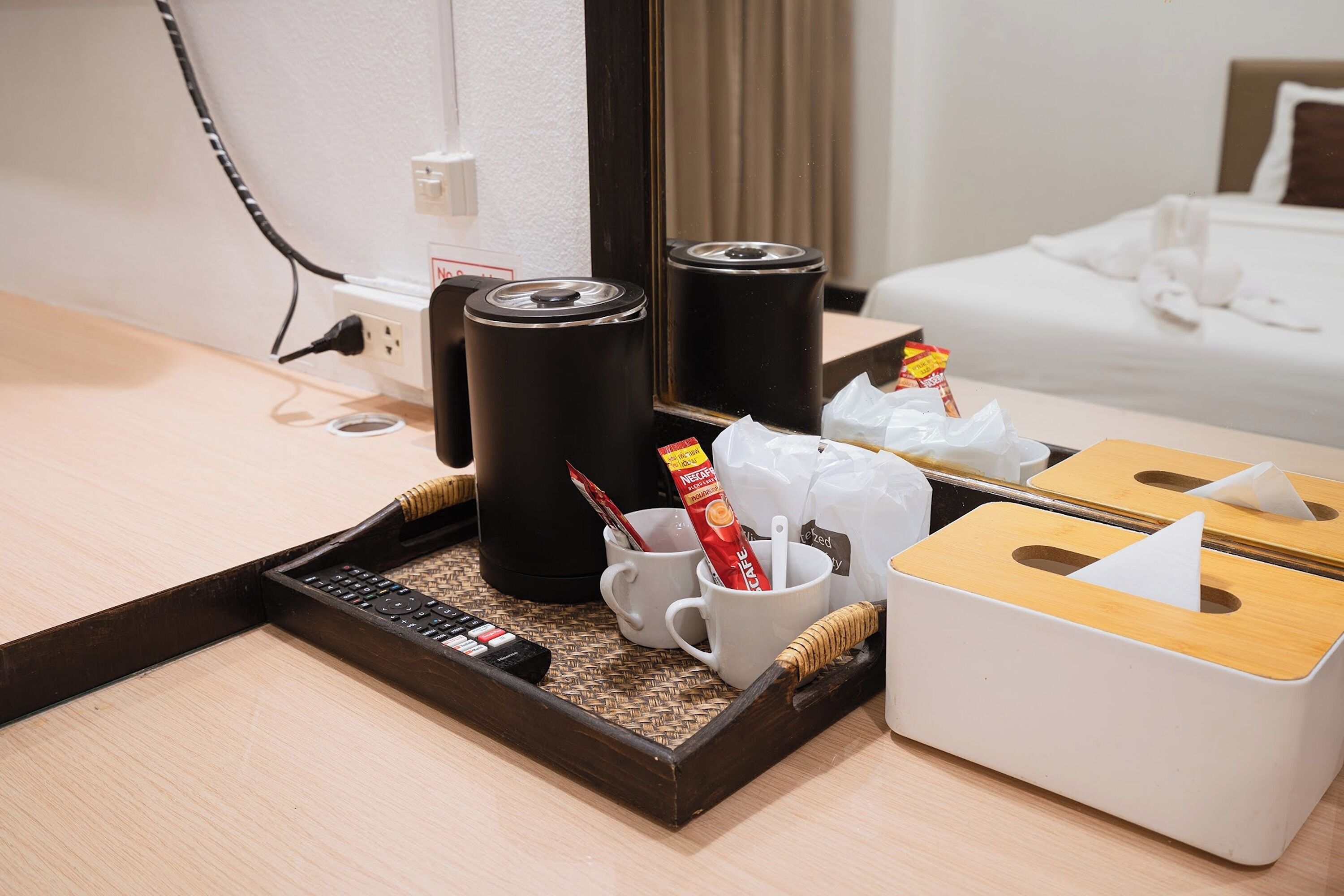 A hotel room with a wooden tray containing a remote control, a white mug, a Nescafé coffee sachet, and a tissue box.