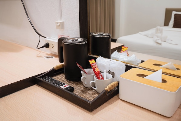 A hotel room with a wooden tray containing a remote control, a white mug, a Nescafé coffee sachet, and a tissue box.