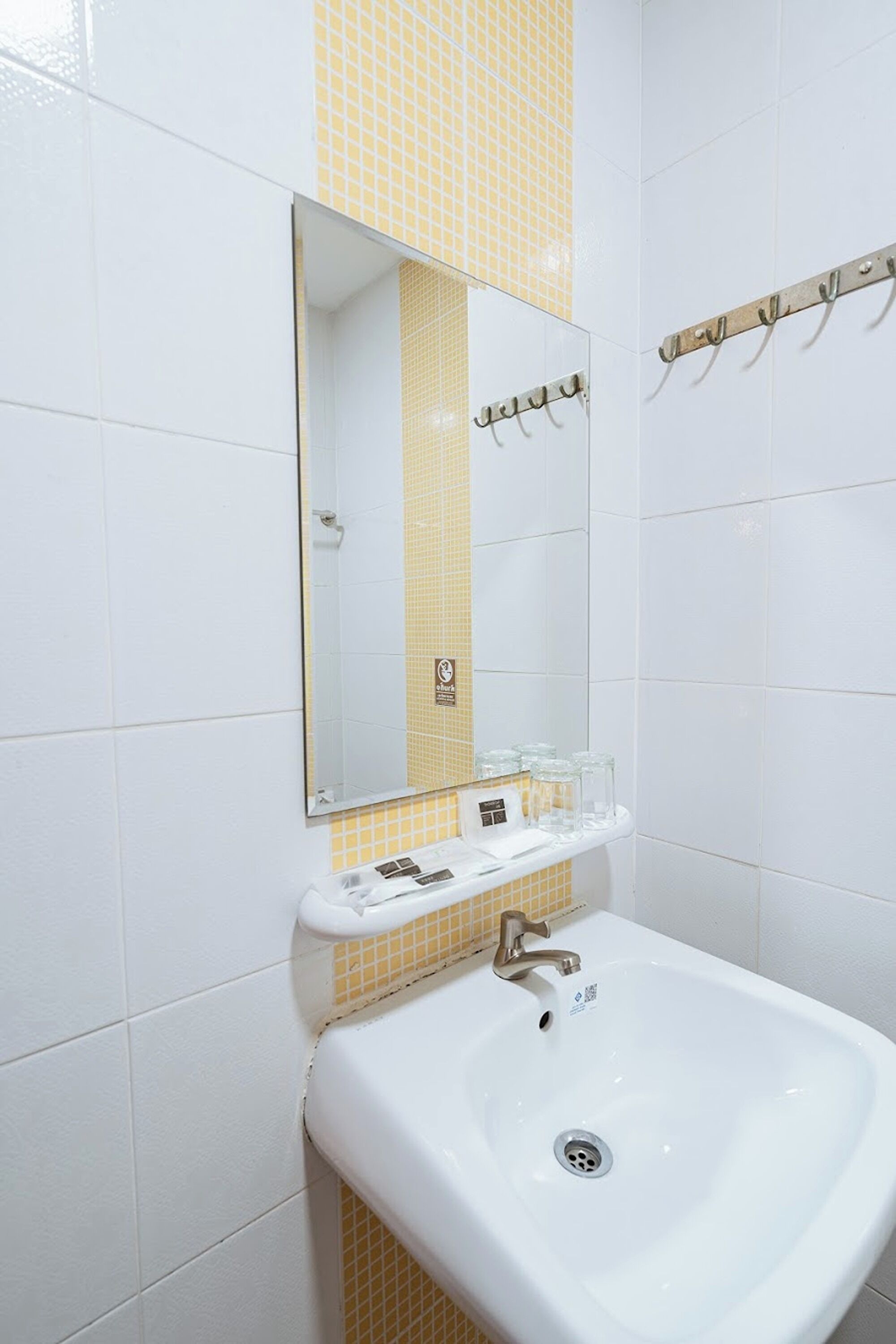 Un baño con lavamanos blanco, un espejo y un perchero para toallas.