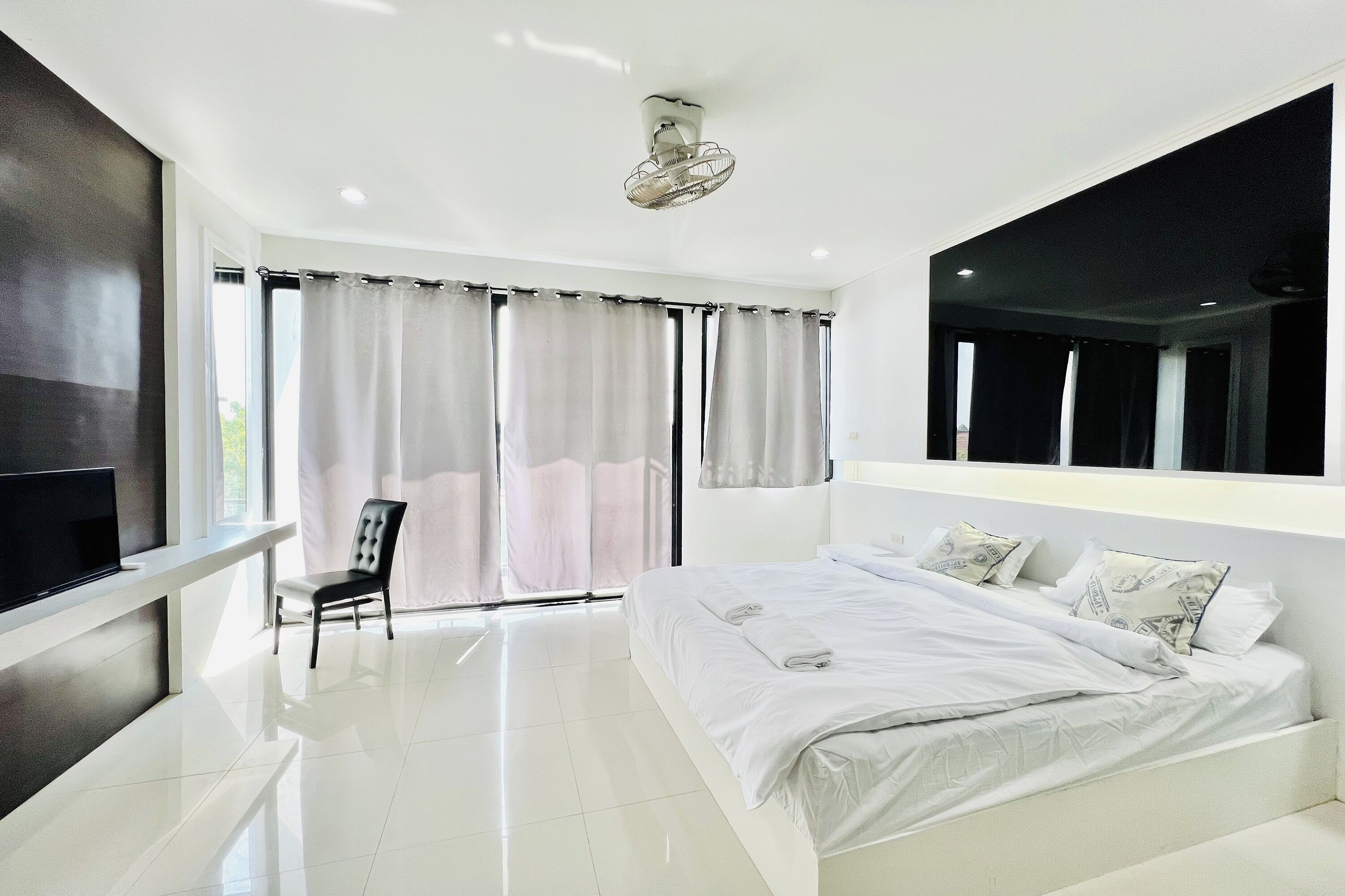 Un dormitorio moderno con una cama grande, un televisor sobre un mueble, una silla y un ventilador de techo.