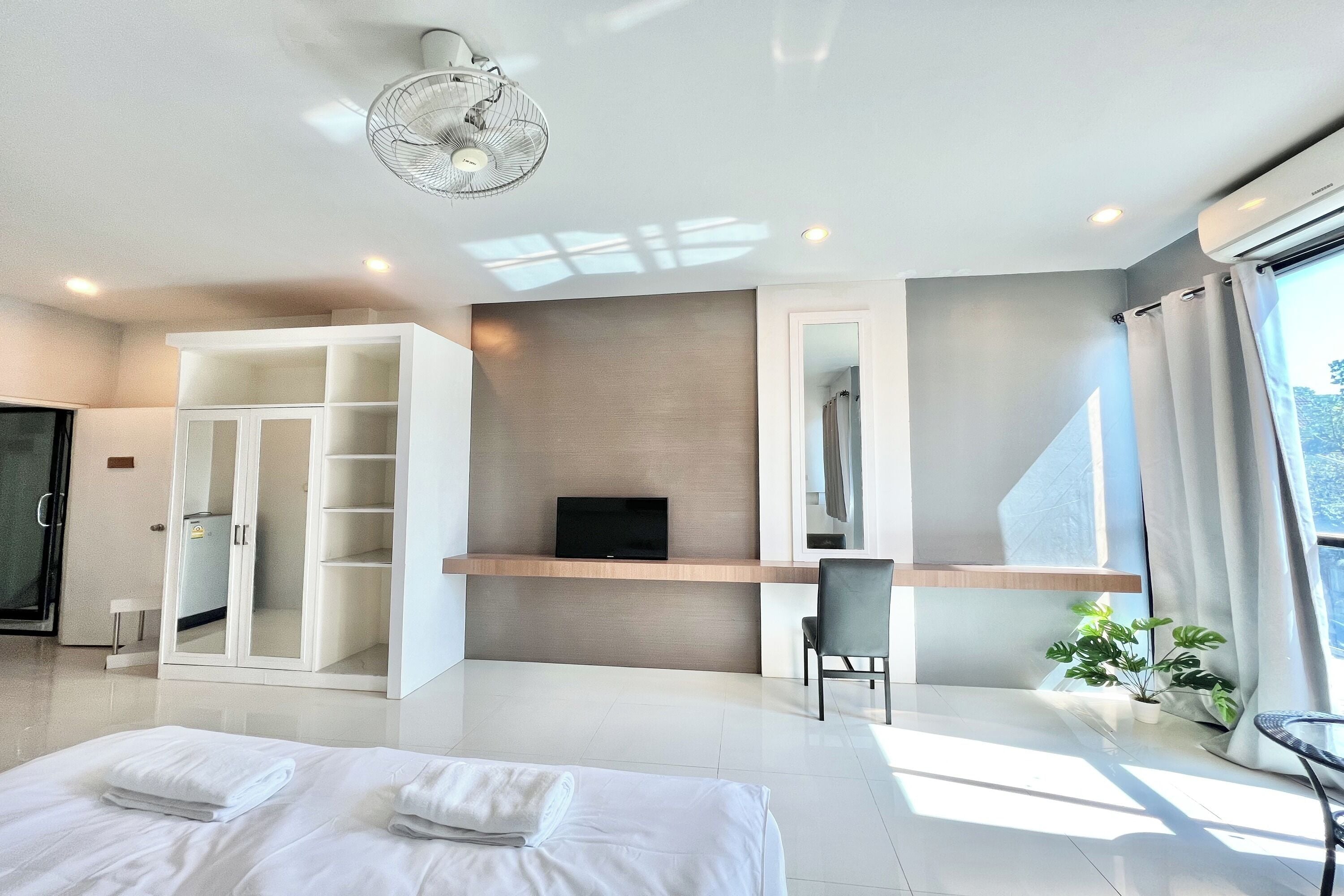 A modern hotel room with a bed, a TV, a wardrobe, a desk, and a chair.