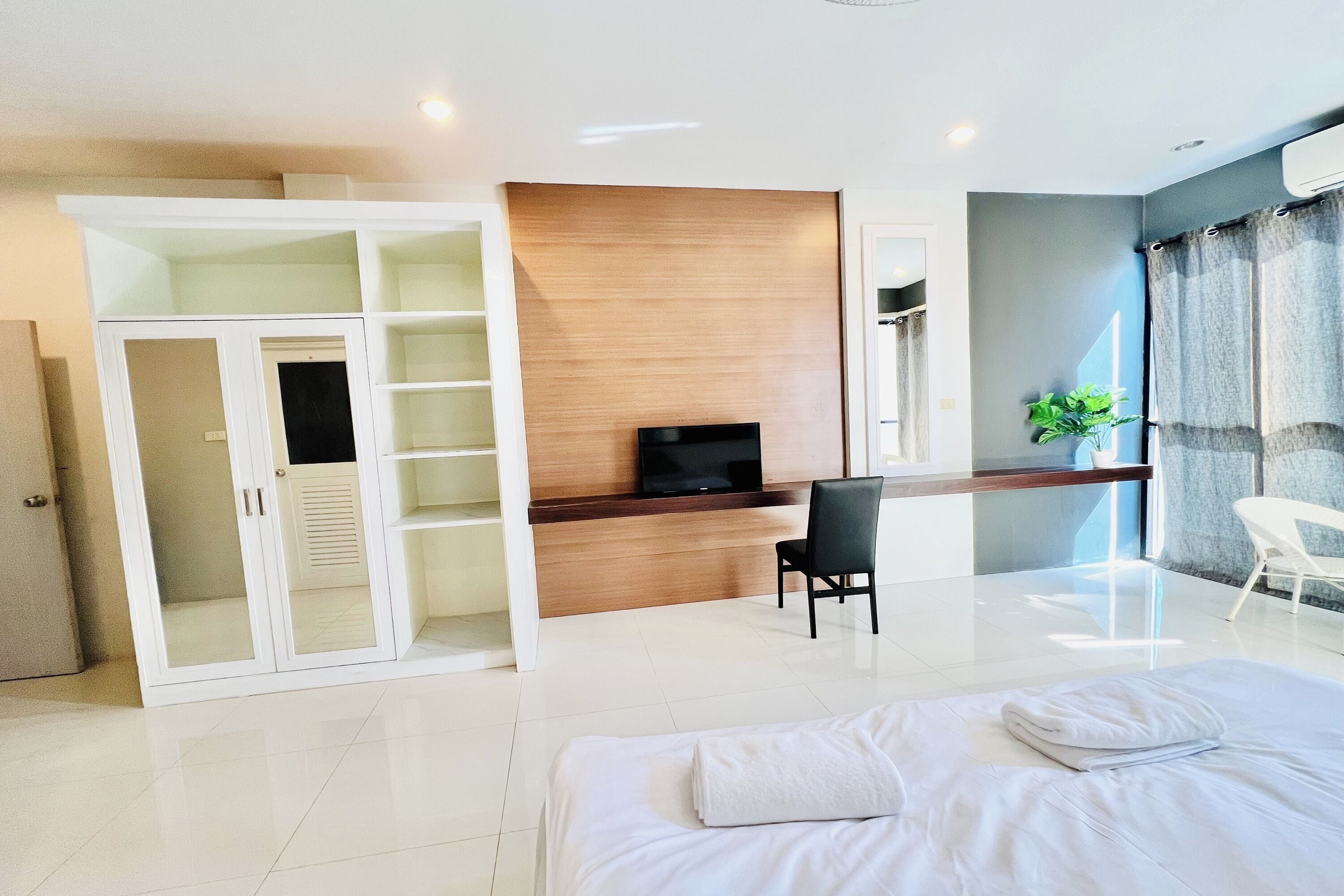 A modern hotel room with a bed, a desk with a TV, a wardrobe, and a seating area.