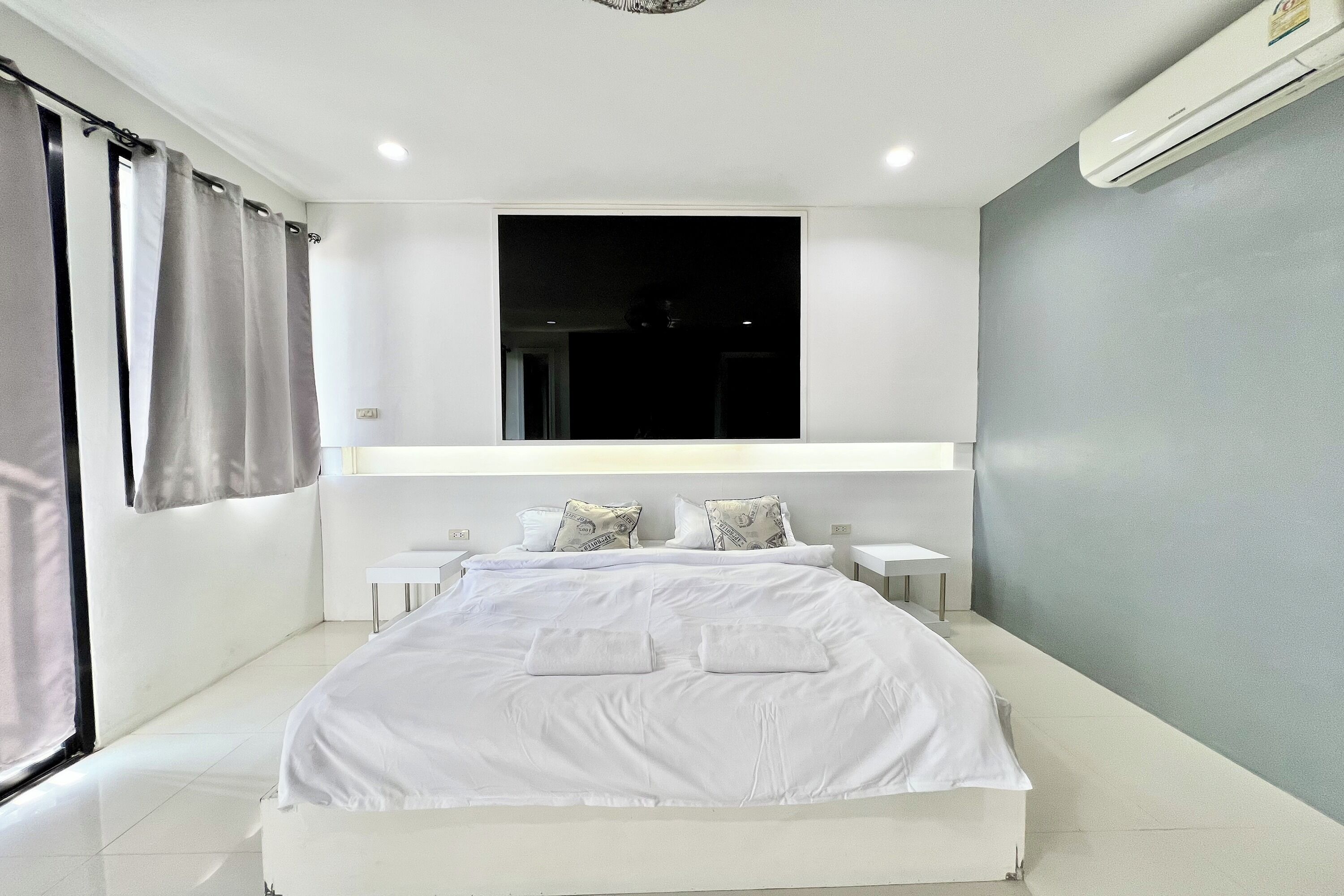 Une chambre moderne avec un grand lit, une table de chevet, une petite table, une fenêtre avec des rideaux et un appareil de climatisation.