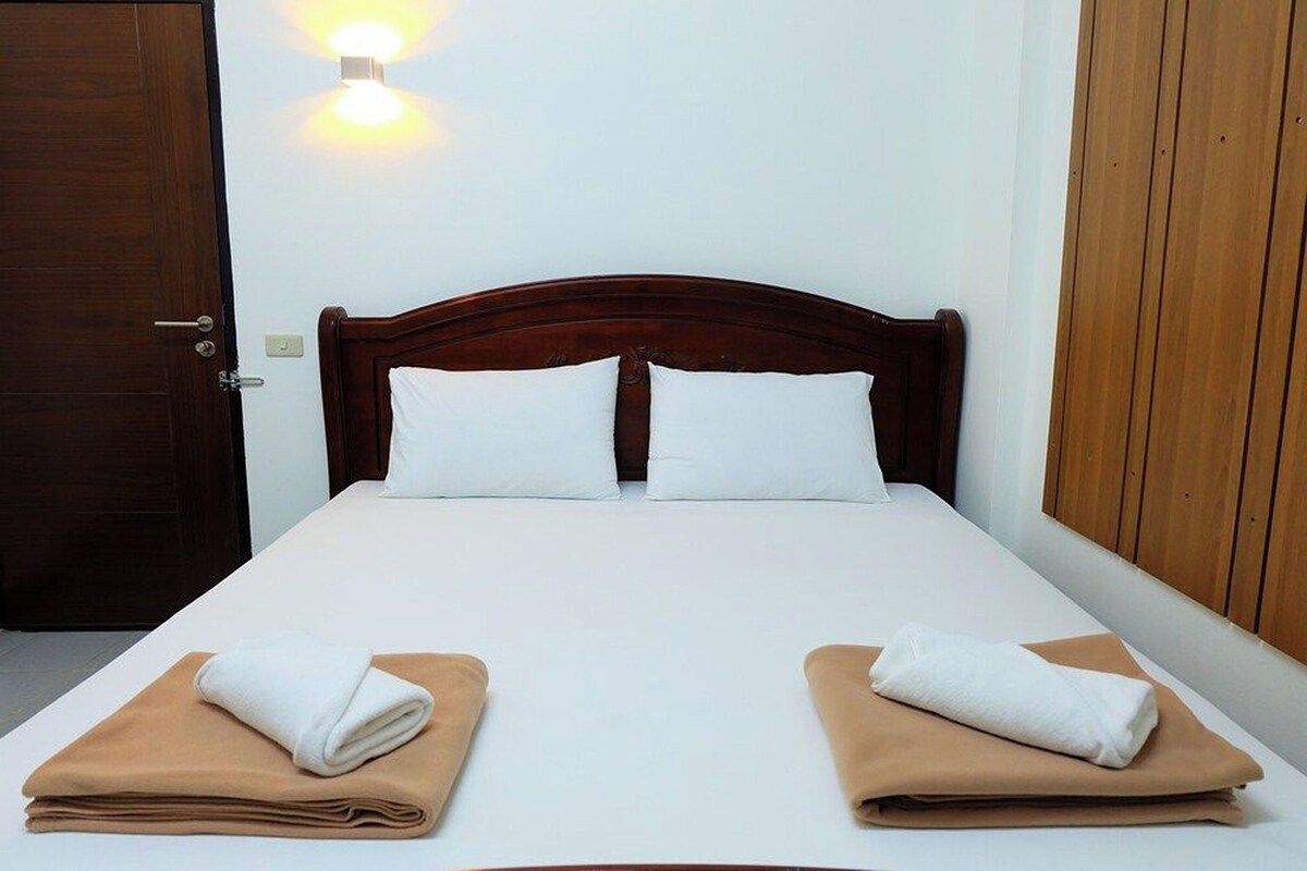 Una cama bien hecha con sábanas blancas y dos toallas dobladas sobre un cubrecolchón marrón.