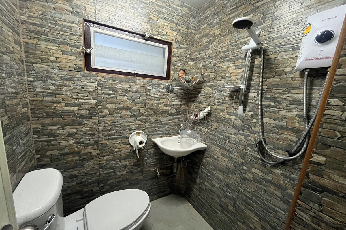 A bathroom with a stone wall, a toilet, a sink, and a shower.