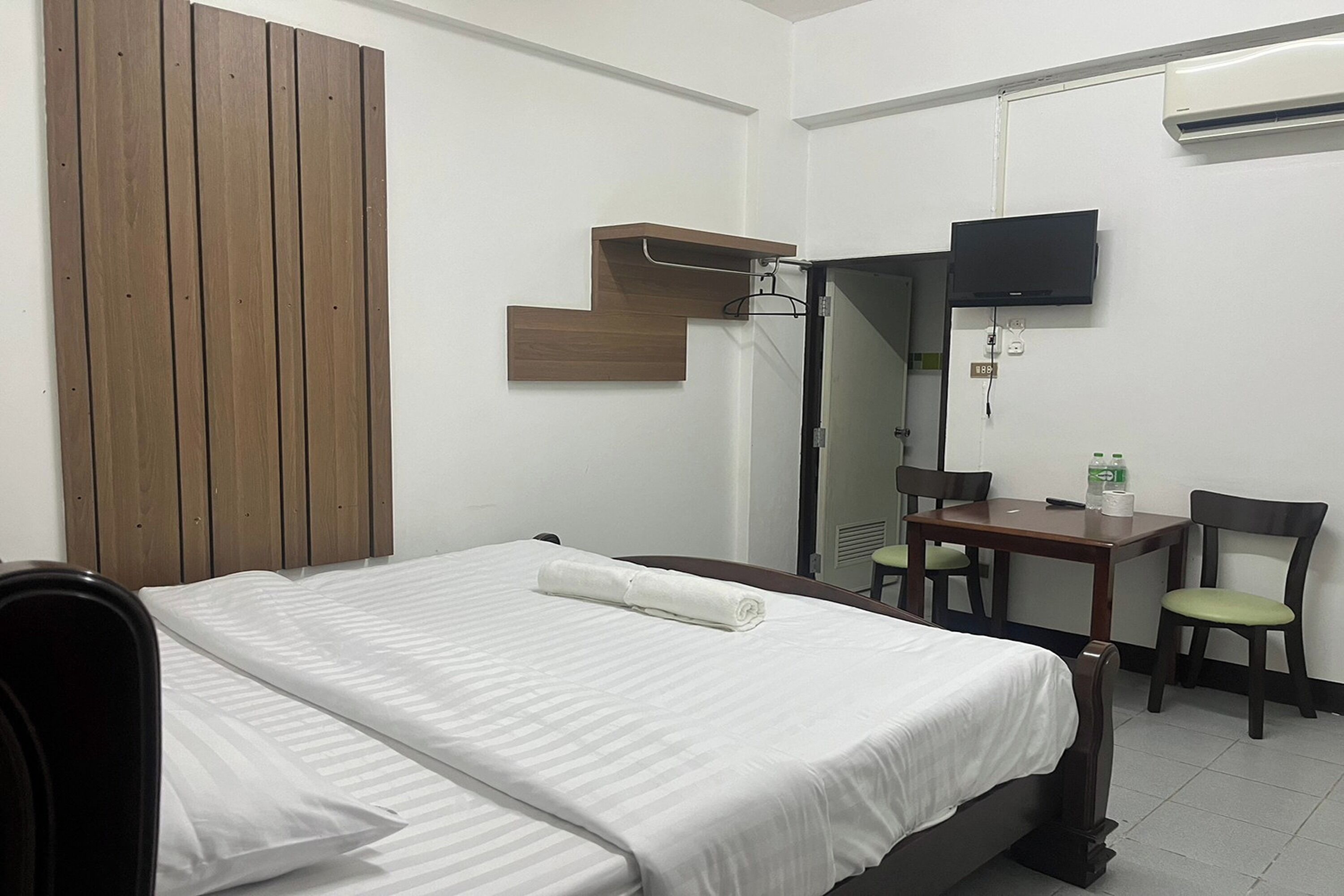 Une chambre d’hôtel comprenant un lit, un bureau, deux chaises, une télévision et un panneau en bois au mur.