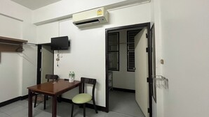 A small, clean room with a wooden table, two chairs, a television, and an air conditioning unit. - Baan Rao Boutique Residence (Chiang Mai)
