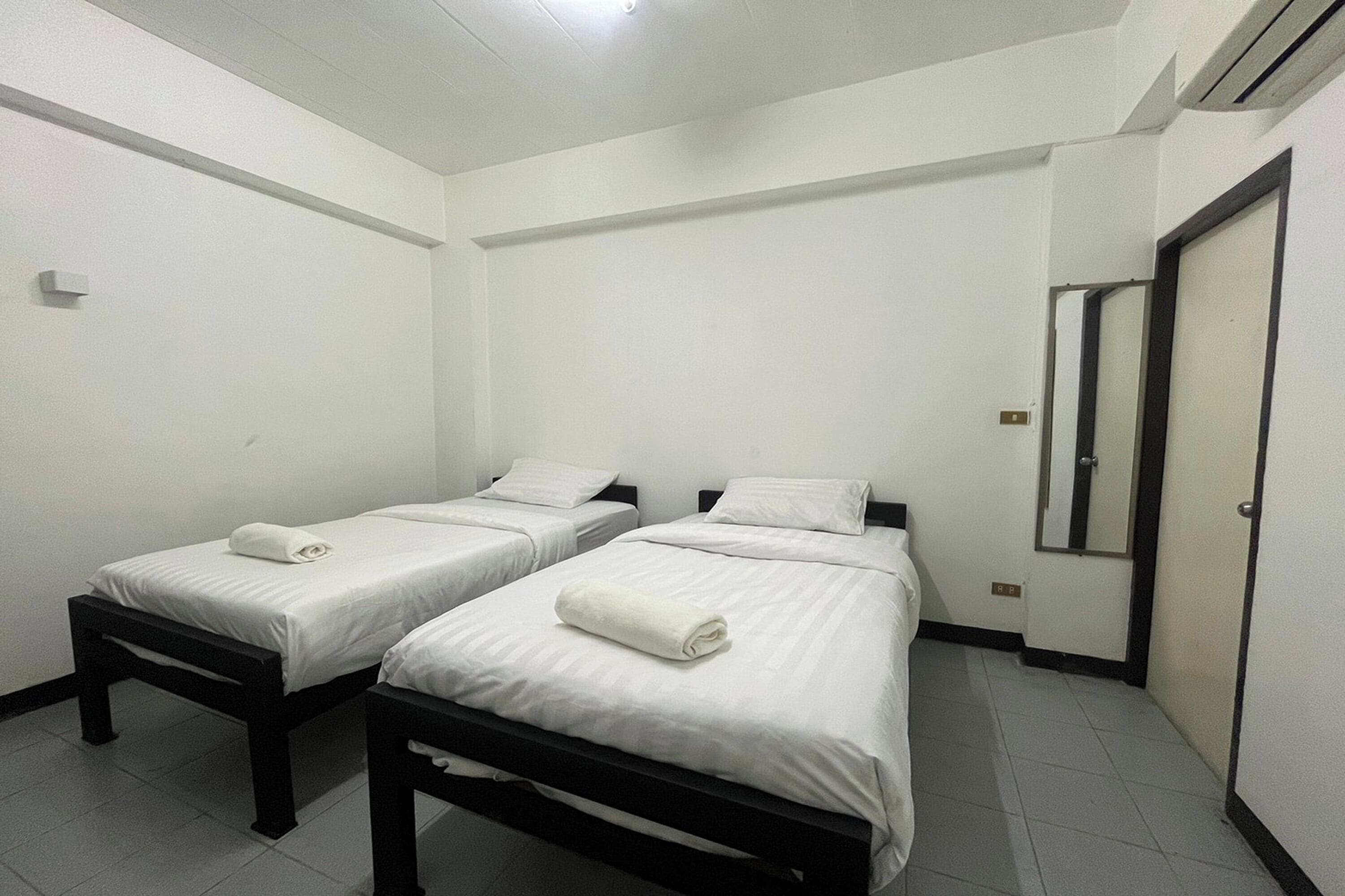 A room with two single beds, white bedding, a mirror, and a door.