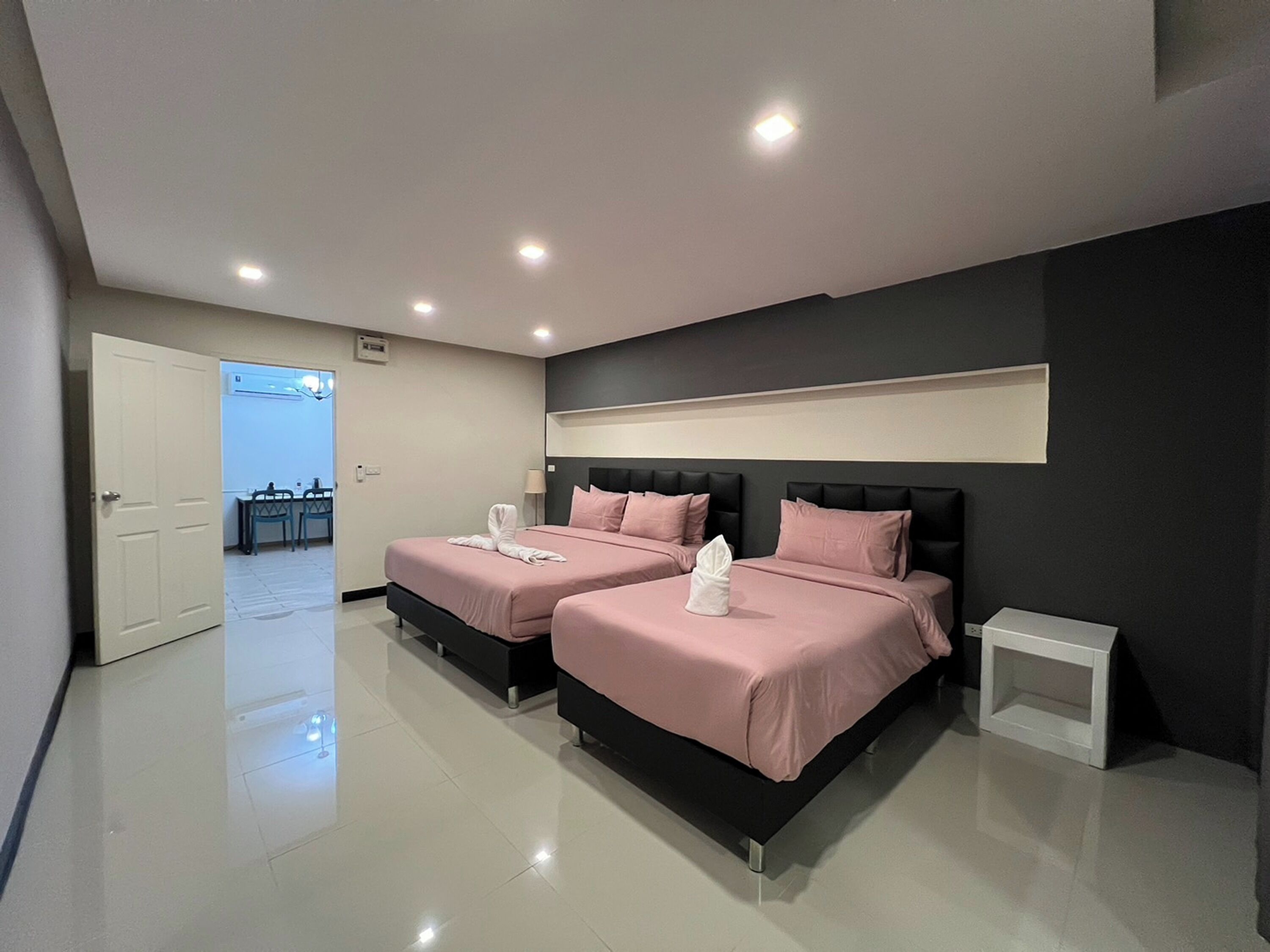 A modern hotel room with two beds, a small bedside table, and a view of the hallway.
