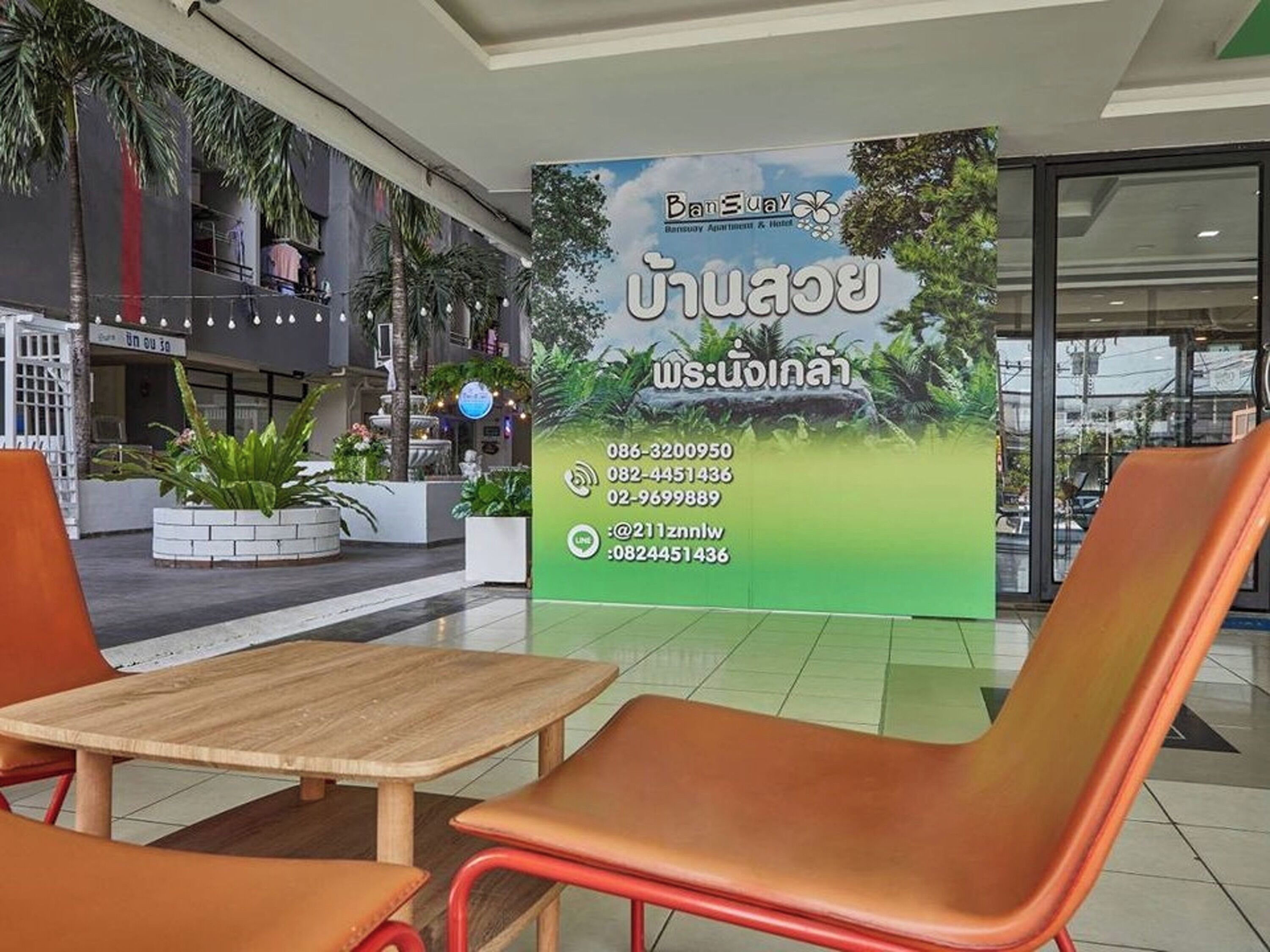 A hotel lobby with a large sign displaying contact information and a view of the outdoor area with plants and a fountain.
