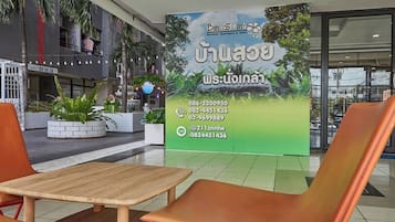 A hotel lobby with a large sign displaying contact information and a view of the outdoor area with plants and a fountain.